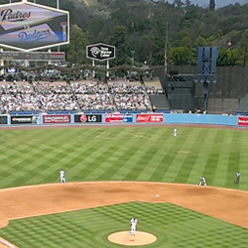 A baseball game in progress at a large stadium filled with fans, featuring advertisements and scoreboards in the background and a view of the field.