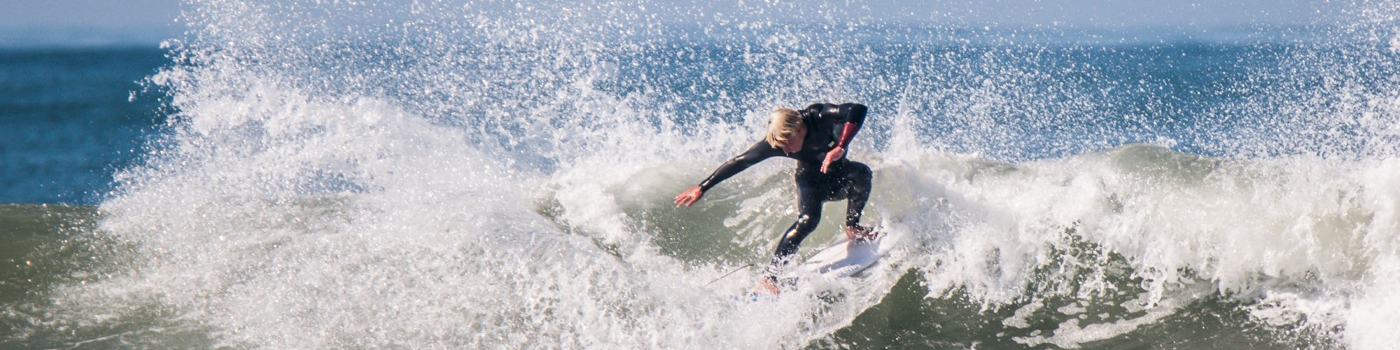 A person is surfing on a large wave, creating splashes of water with their skillful maneuver. The ocean and sky form the backdrop.