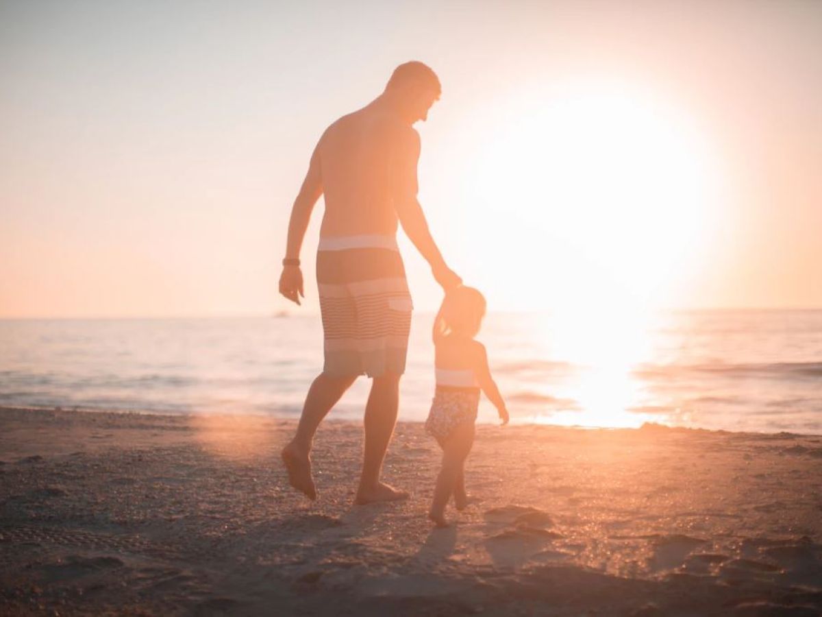 A person and a child are walking on the beach at sunset, holding hands and enjoying the serene moment together.