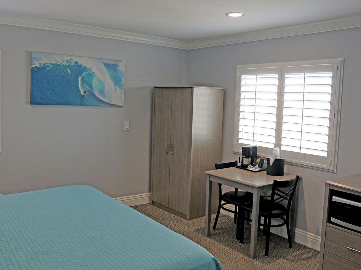 A tidy bedroom with a bed, wardrobe, desk with chairs, wall art, and windows with shutters. A TV is mounted on the wall.