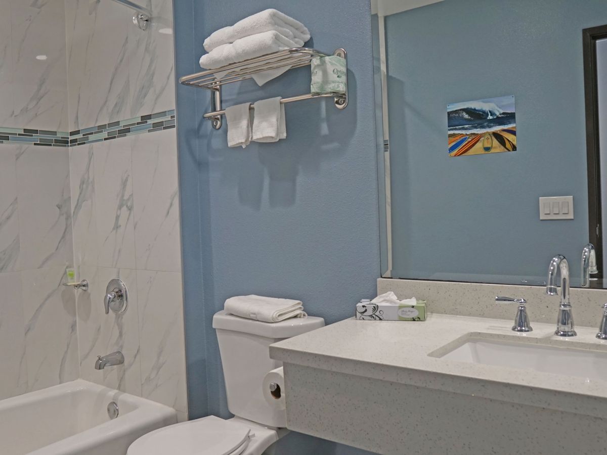 A modern bathroom with a toilet, sink, marble bathtub, towels on a rack, and a wall-mounted mirror. White and blue color scheme throughout.