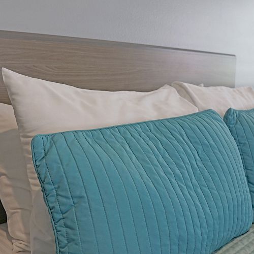 The image shows a bed with a wooden headboard, white pillows, and teal cushion covers arranged neatly, indicating a well-made bed.