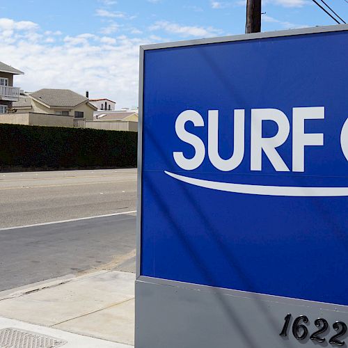 The image shows a sign for Surf City Inn with the address 16220, located next to a road, with houses visible in the background.