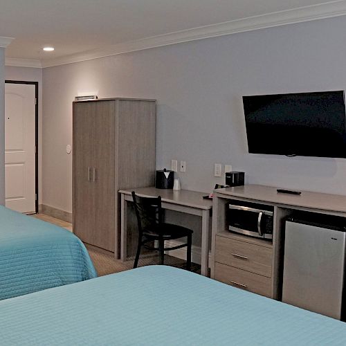 A hotel room with two beds, a flat-screen TV, a wardrobe, a desk with a chair, and appliances like a microwave and mini-fridge is depicted.