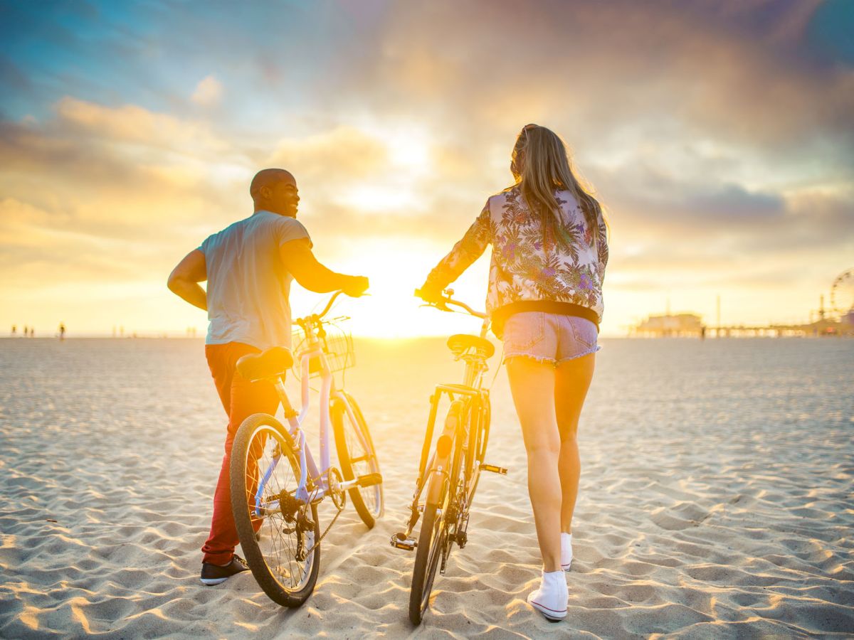 Two people walking with bicycles on a beach at sunset, with a bright horizon and a peaceful atmosphere.