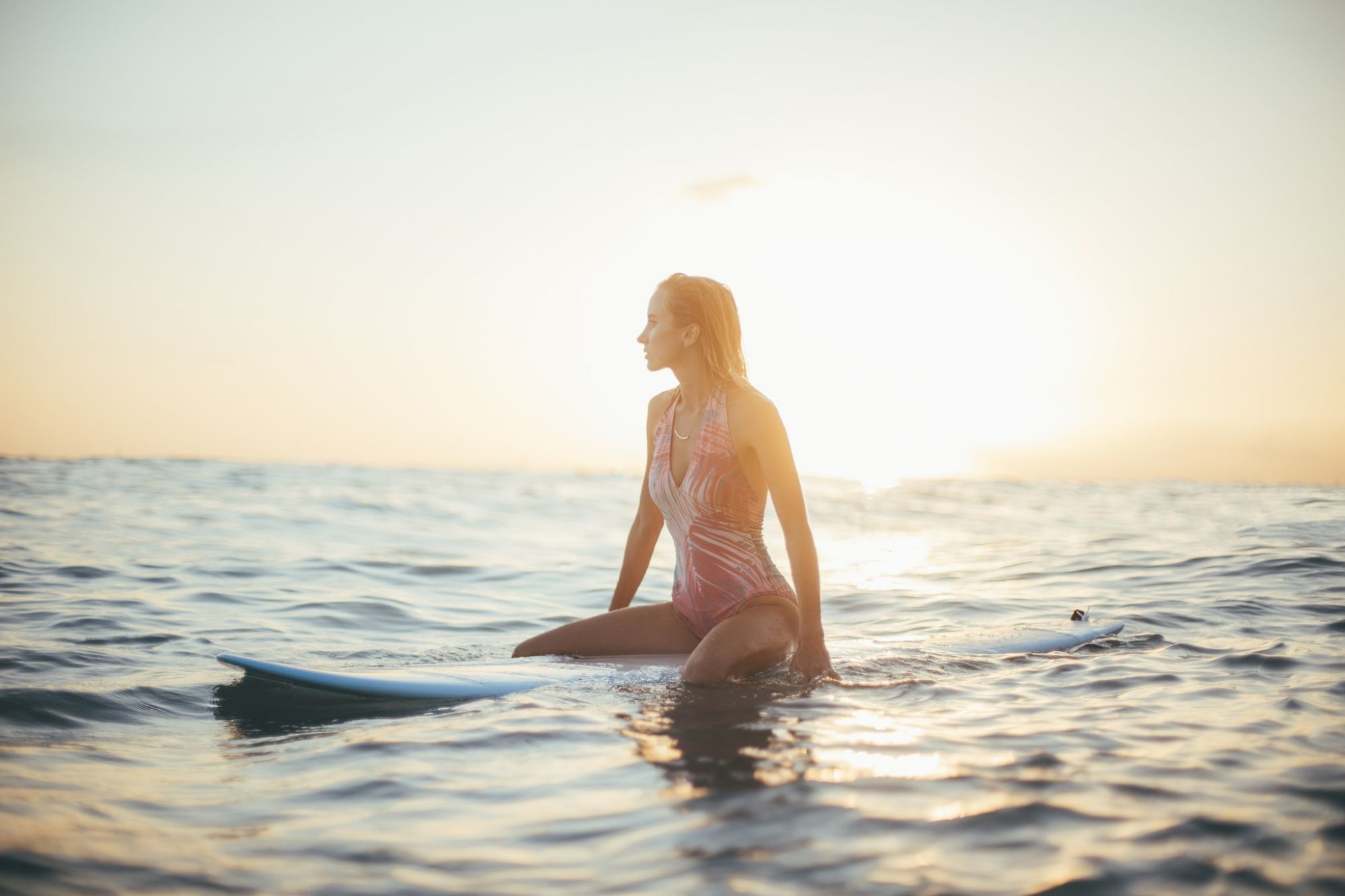 A person sitting on a surfboard in the ocean, with the sun setting in the background, creating a serene and picturesque scene.