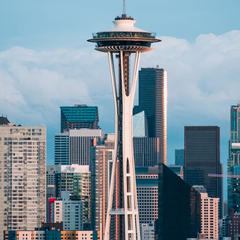 The image shows the Space Needle with surrounding skyscrapers in Seattle, under a sky with clouds.