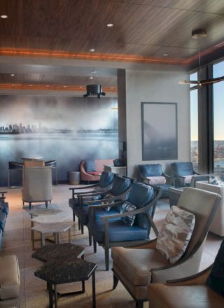 The image depicts a modern lounge area with comfortable seating, city skyline art on the wall, and large windows offering a scenic view of a Ferris wheel.
