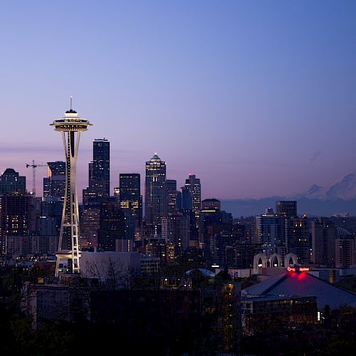 The image shows the Seattle skyline at twilight, featuring the Space Needle prominently, with Mount Rainier visible in the background.