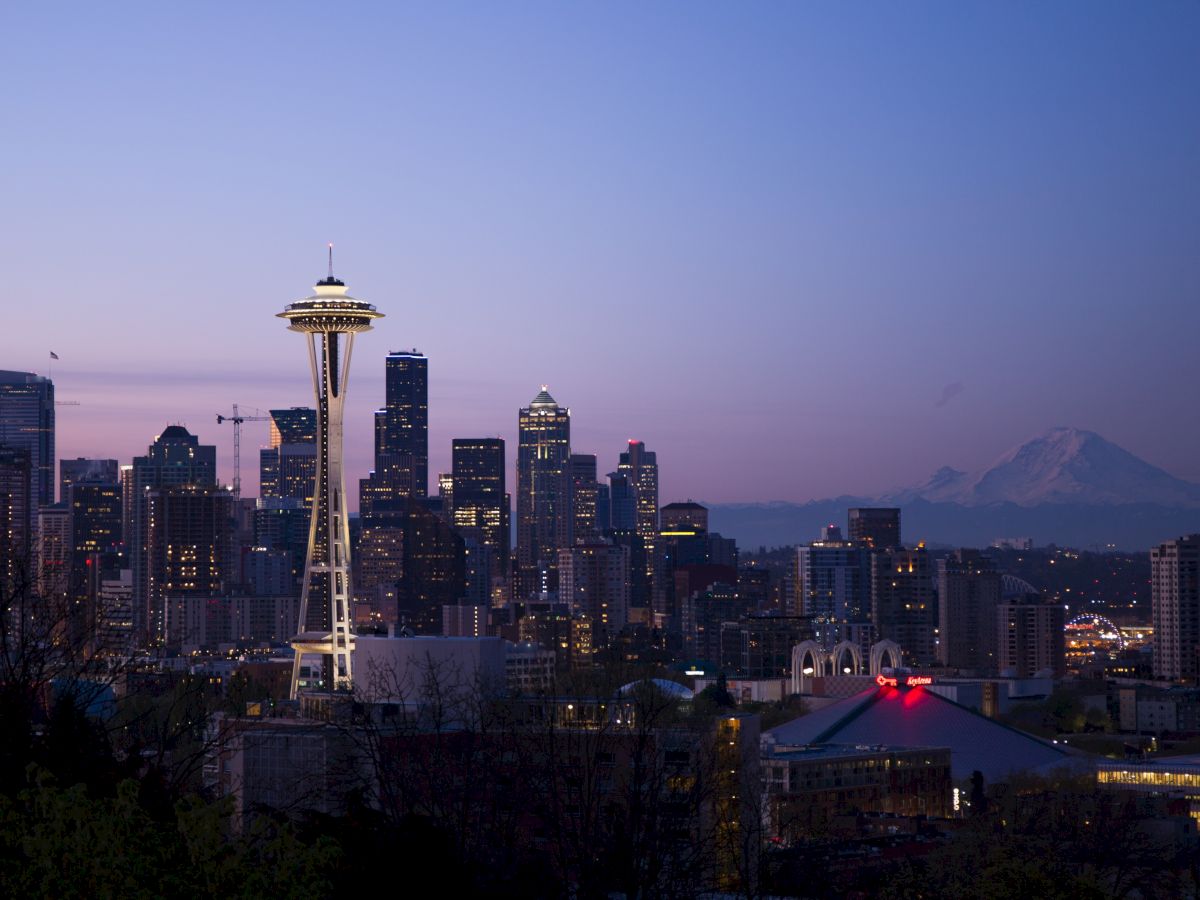 A twilight view of the Seattle skyline featuring the Space Needle, with Mount Rainier visible in the background against a clear sky.