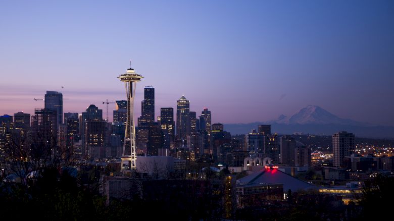 A twilight view of the Seattle skyline featuring the Space Needle, with Mount Rainier visible in the background against a clear sky.