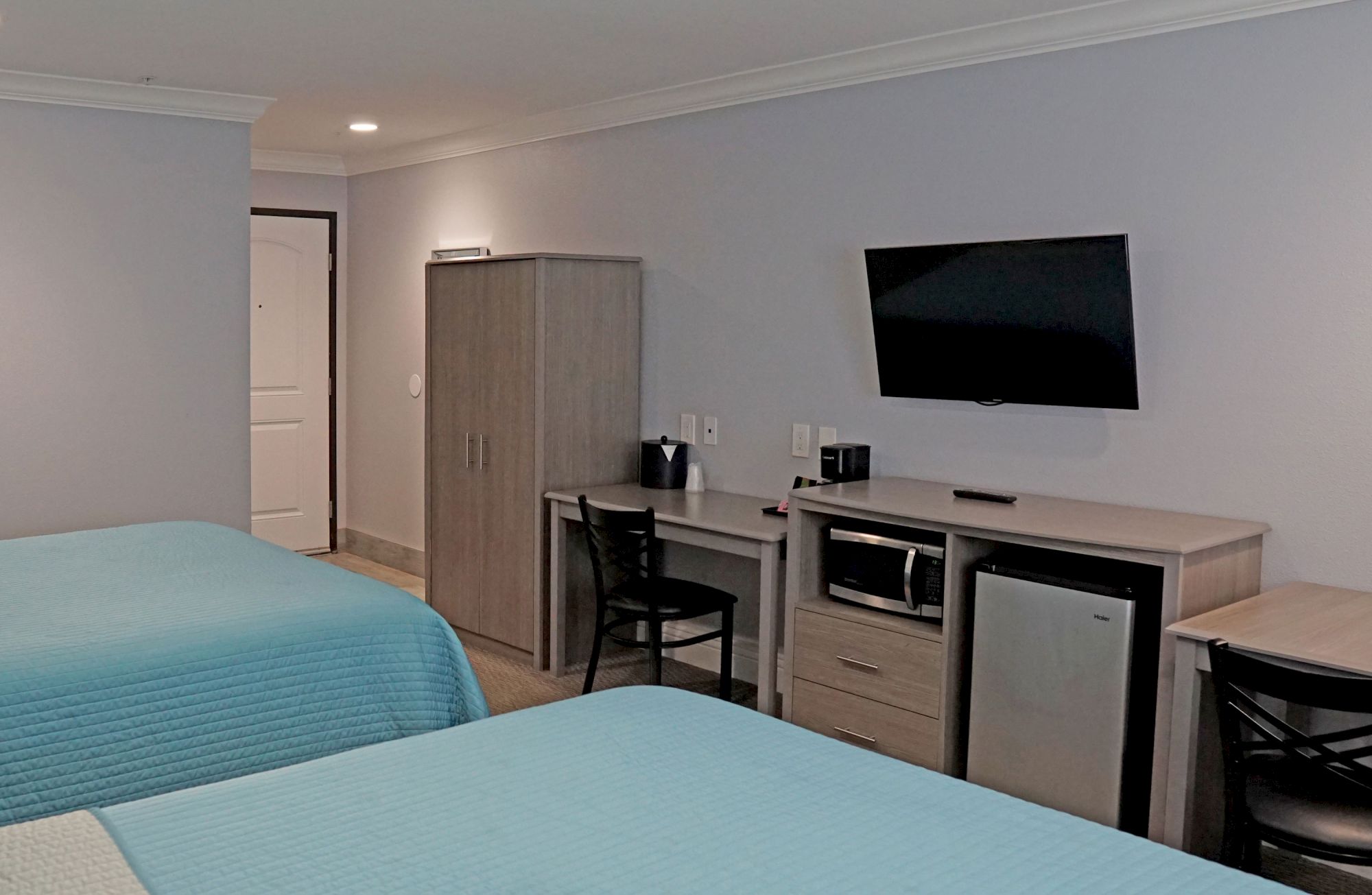 A hotel room with two beds, a desk with a chair, a flat-screen TV mounted on the wall, a mini-fridge, and a microwave is depicted.