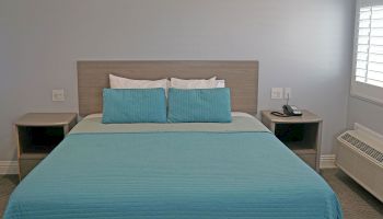 A neatly made bed with blue bedding and matching pillows, flanked by two bedside tables; one holding a phone, within a minimalist room.