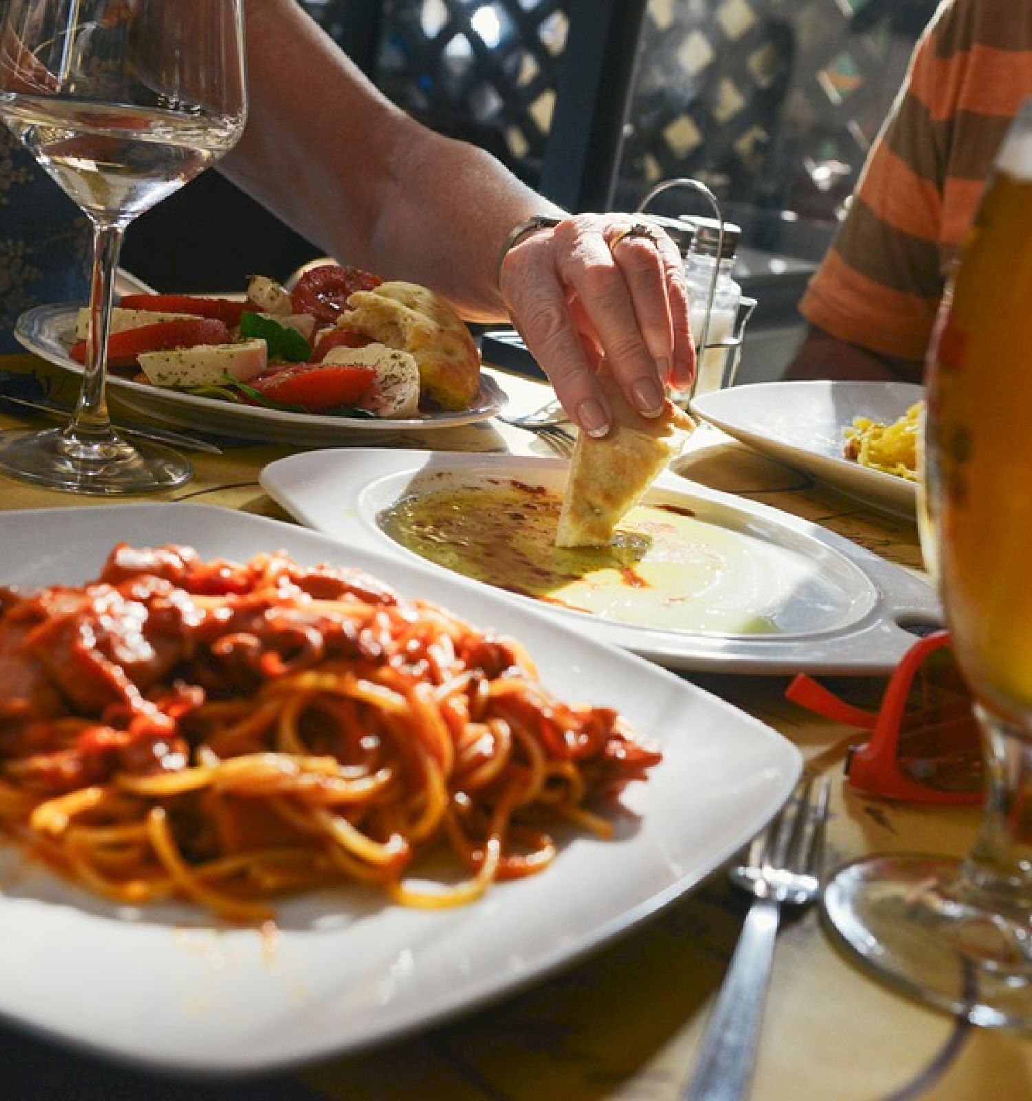 People dining with pasta, bread dipped in olive oil, salad, and drinks including beer and wine, creating a cozy and inviting atmosphere.