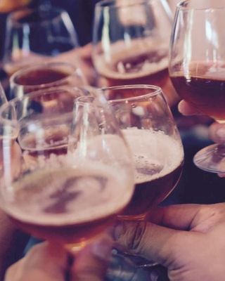 People clinking glasses filled with a golden-colored beverage, likely beer or a similar drink, creating a celebratory atmosphere.